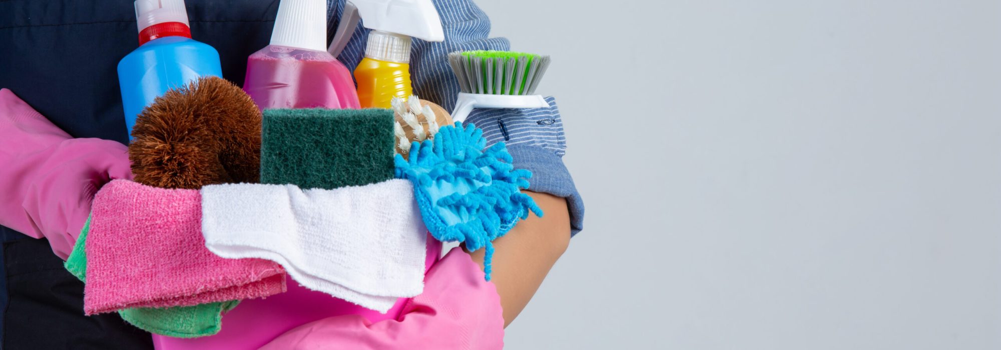 Young girl is holding cleaning product, gloves and rags in the basin on white background